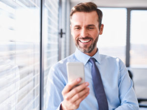 Happy businessman using his smartphone standing at office