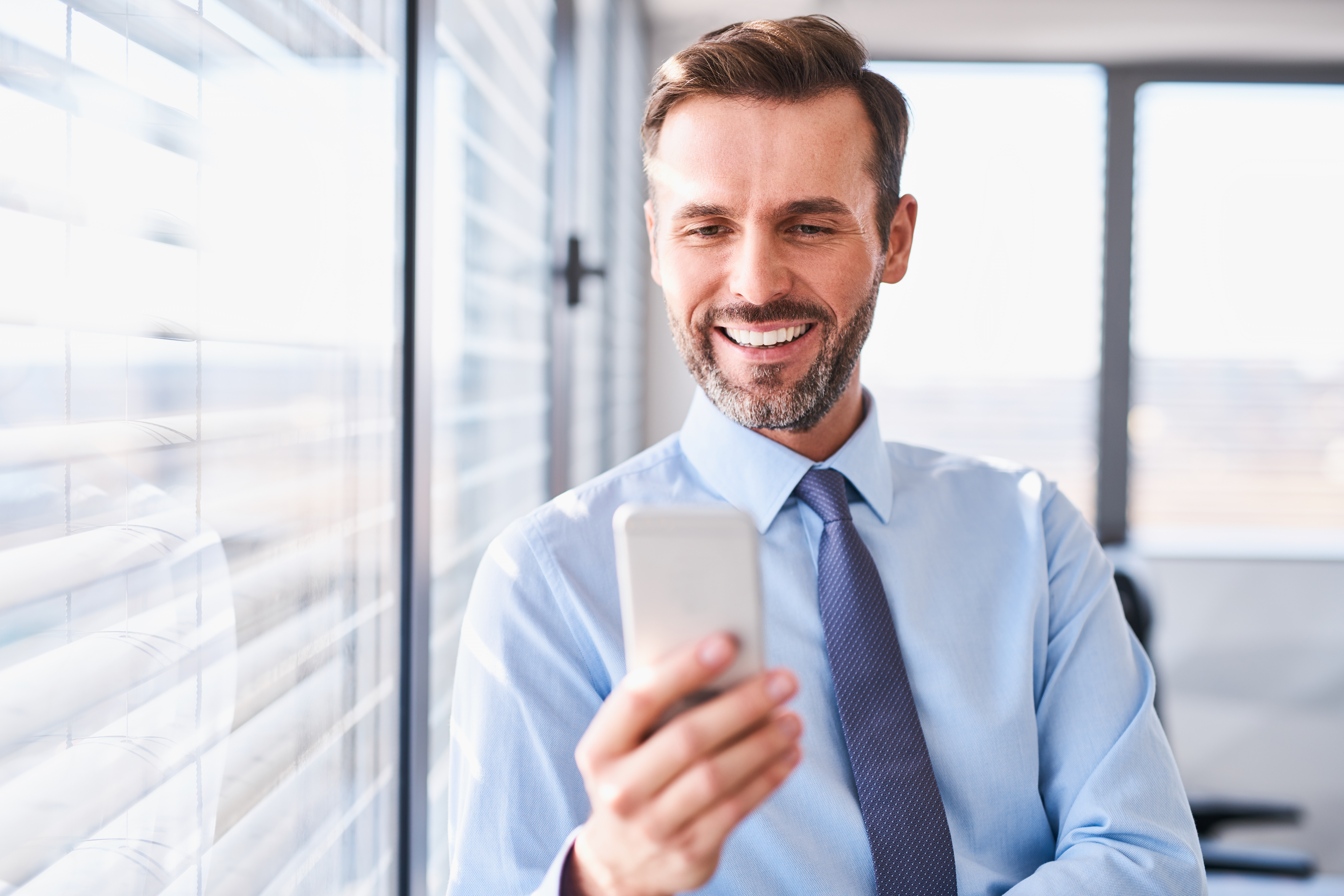 Happy businessman using his smartphone standing at office